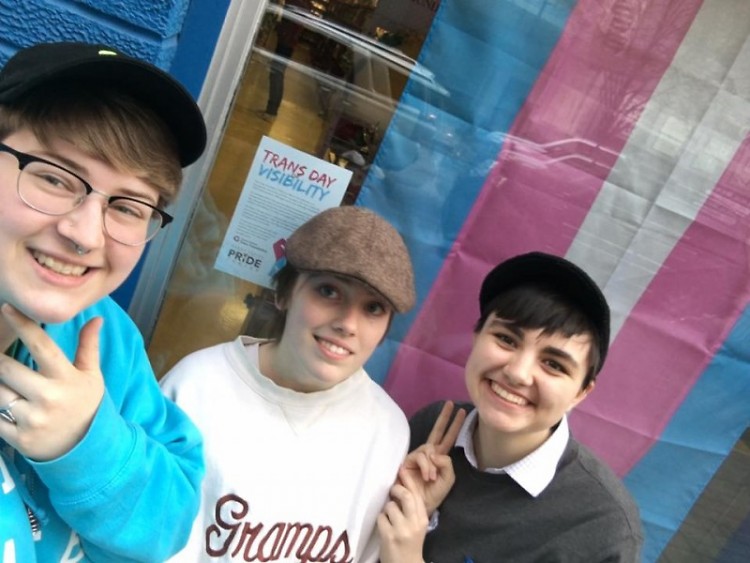 Three trans individuals pose with a transgender pride flag in downtown GR.