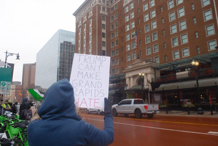 A protester holding a sign that reads 'TRUMP CAN'T MAKE GRAND RAPIDS HATE,' seen across the street from the Amway Grand Plaza.