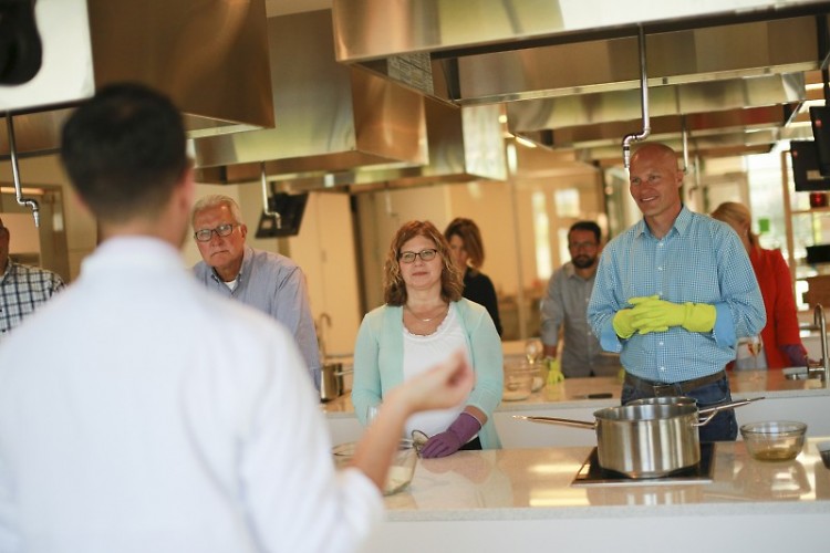 Guests in a class learn about the techniques and history of the dish they are preparing