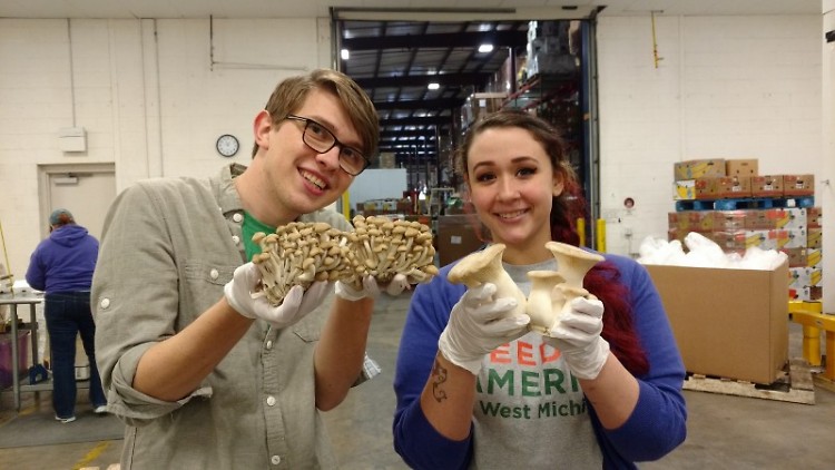 Feeding America West Michigan staff members Josiah Kinney and Francesca Almonte display mushrooms donated by GMI.