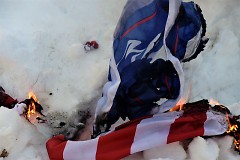 What is left of a burned Trump and American flag lay smoldering in the snow on Saturday, January 20, 2018.