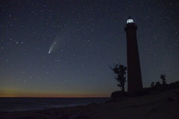 A view of a comet shooting through the sky next to a lighthouse.